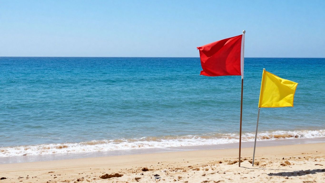Red and yellow flags on a sunny beach with calm waves.