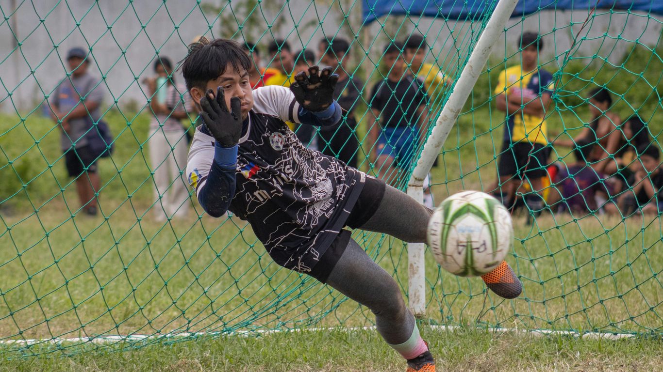 a young boy kicking a soccer ball on top of a field