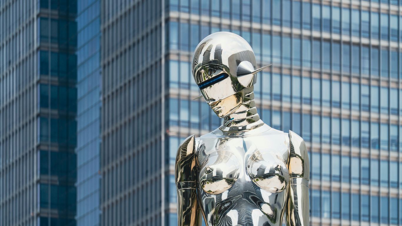 Shiny statue stands in front of a skyscraper.