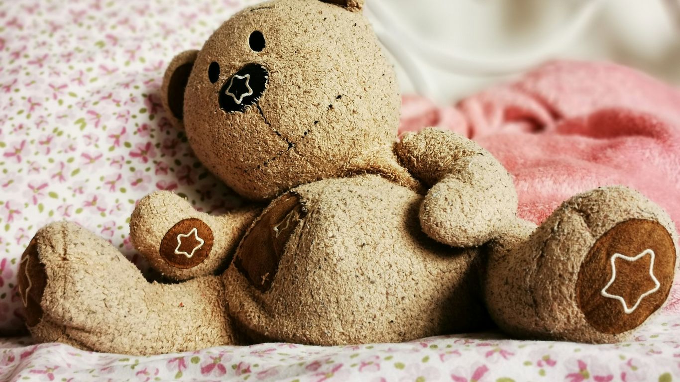 a brown teddy bear sitting on top of a bed