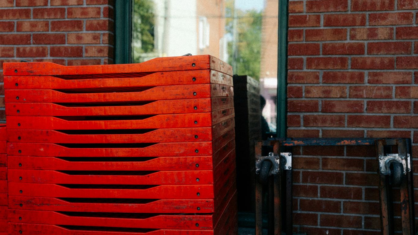 Stack of red plastic trays next to brick wall.