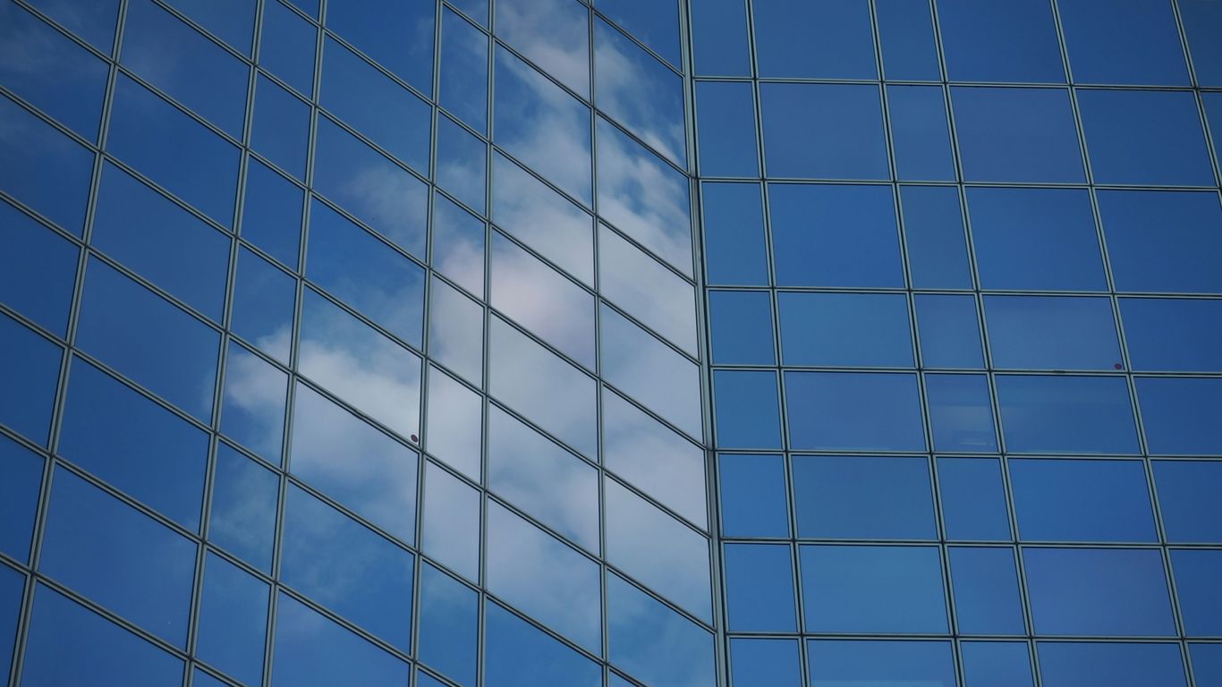 a blue sky and clouds reflected in a glass building