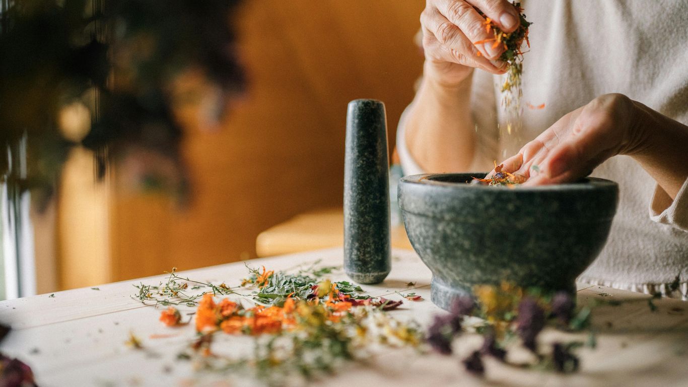 Person preparing dried herbs with mortar and pestle on table.