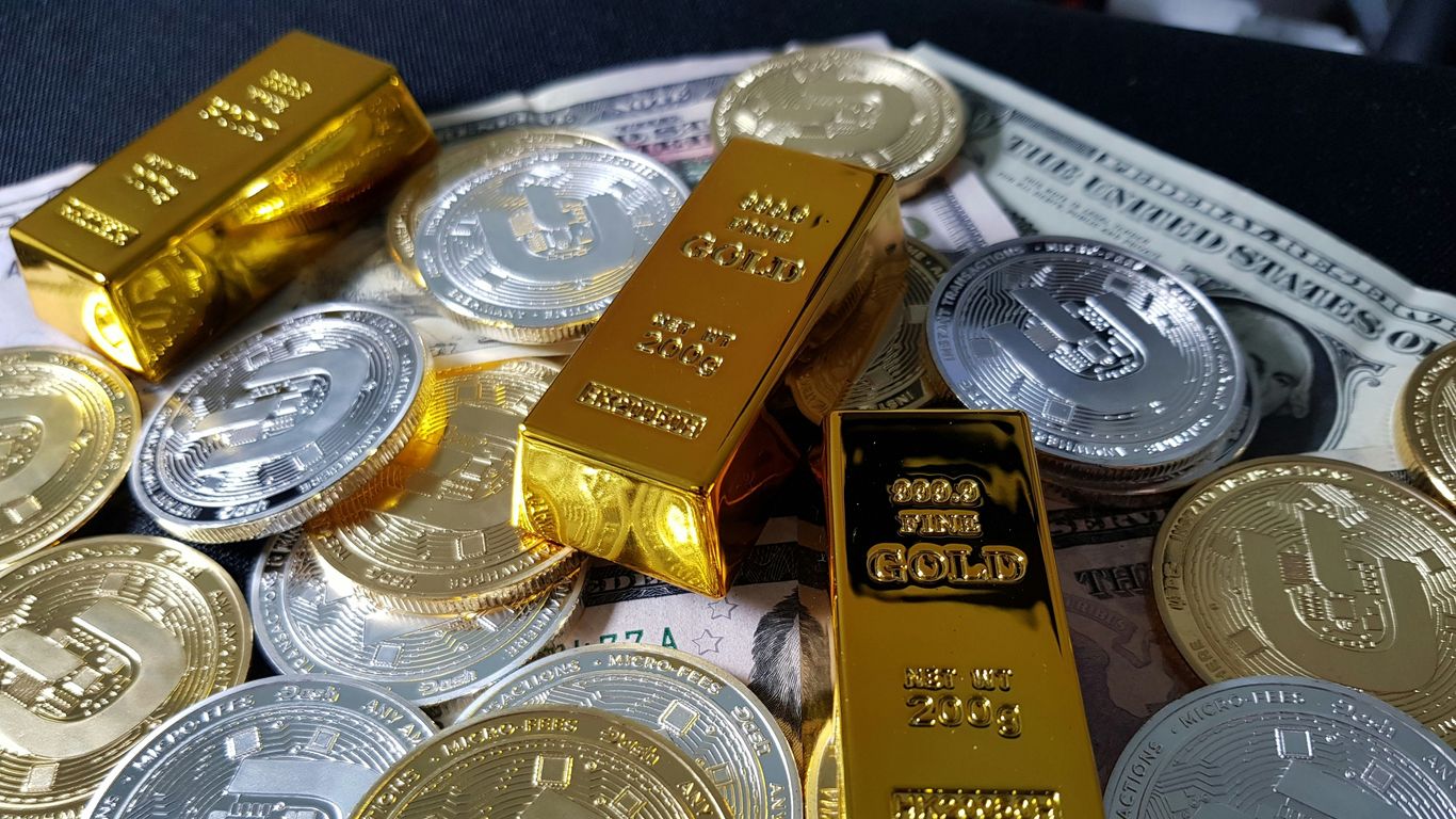 Gold bars and silver coins scattered over dollar bills.