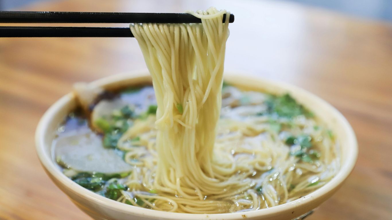 Chopsticks lifting noodles from a bowl of hot noodle soup.