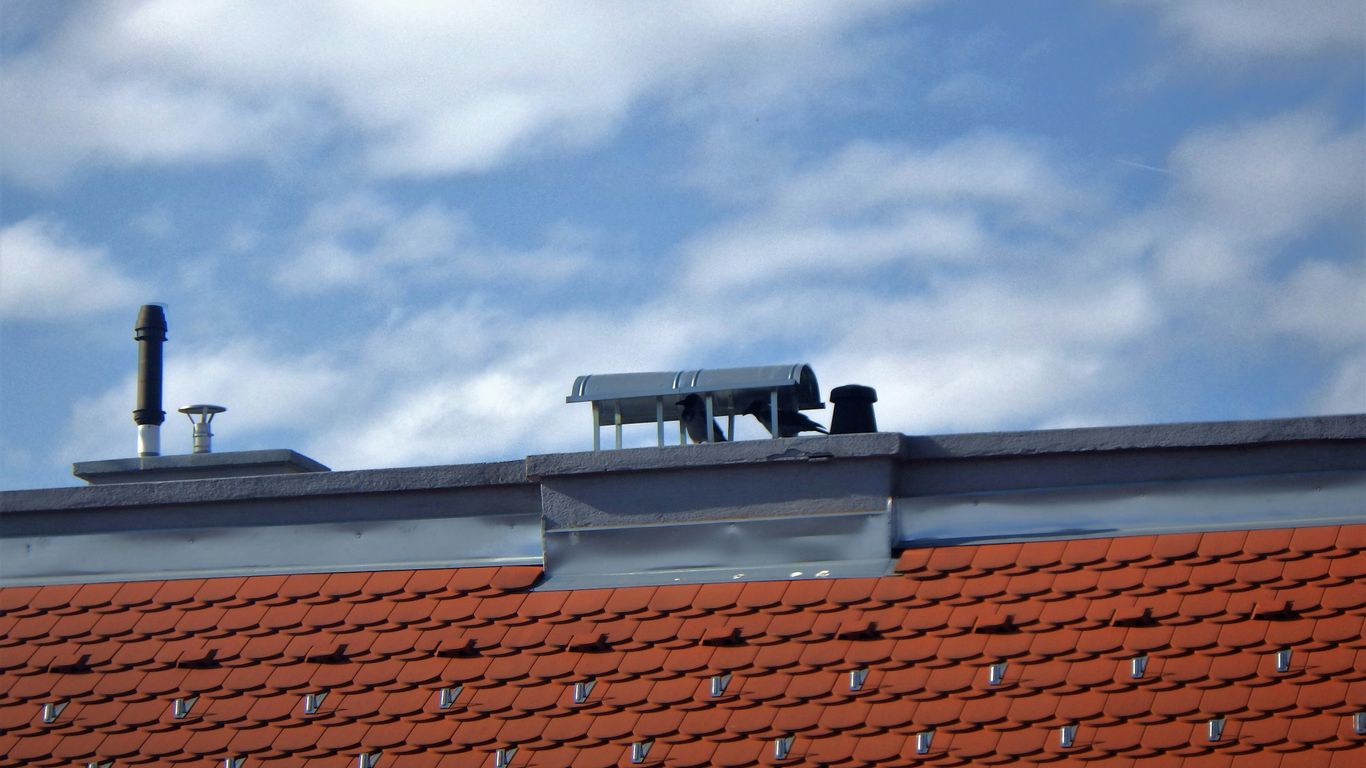 Roof with solar attic fan and passive vents, red tiled surface, and blue sky with clouds, illustrating attic ventilation systems.