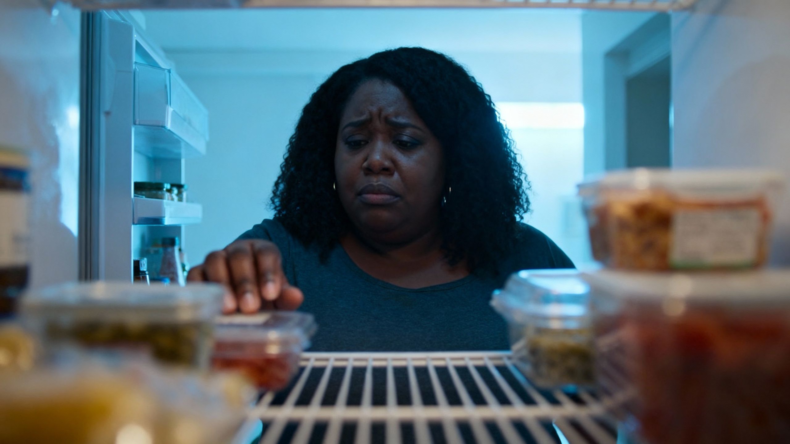Woman looking into a refrigerator, seeking comfort.