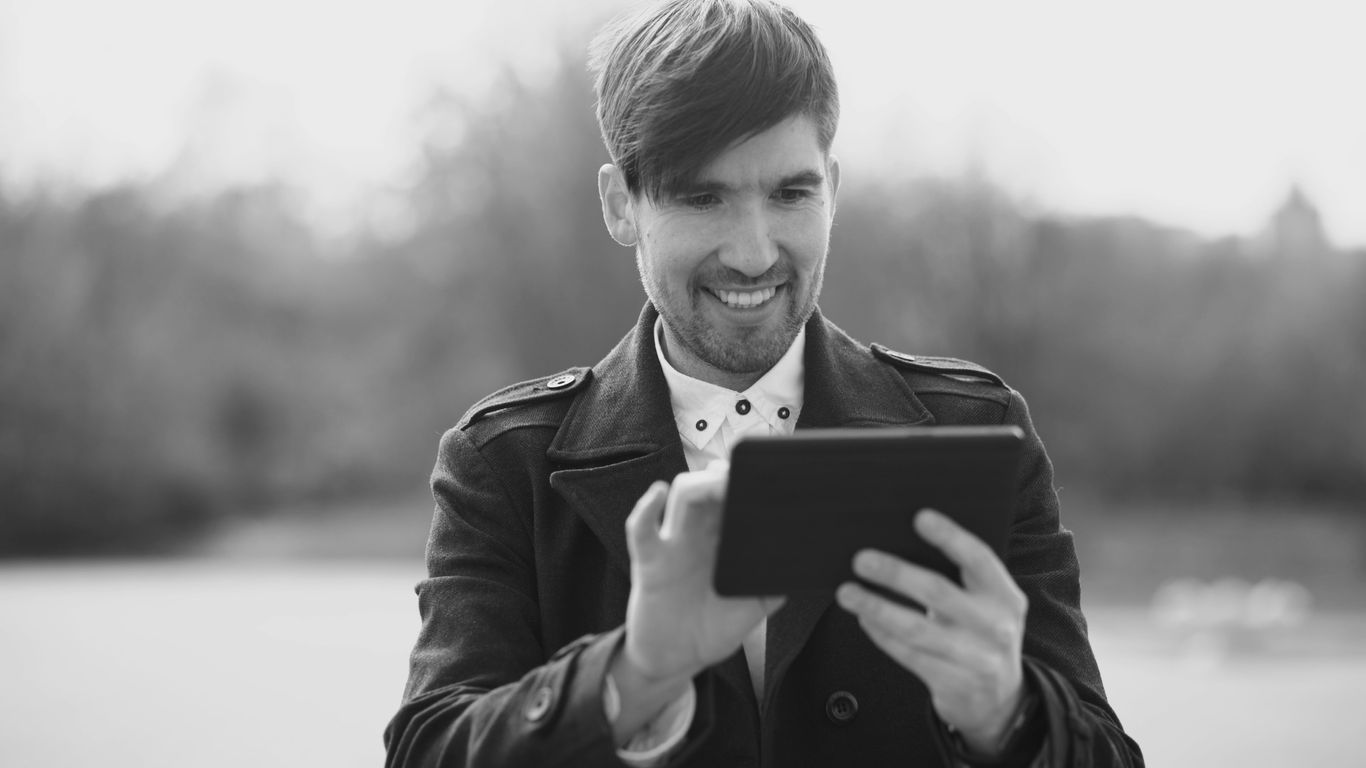 Man smiling while using a tablet outdoors