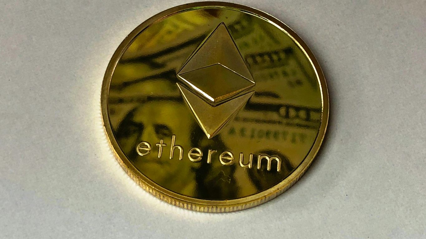 Golden Ethereum coin on a light surface with money in background.