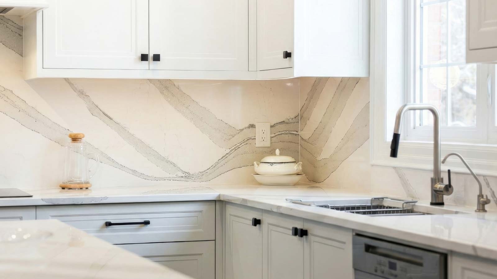 Modern white kitchen with marble countertops and backsplash, stainless steel faucet.