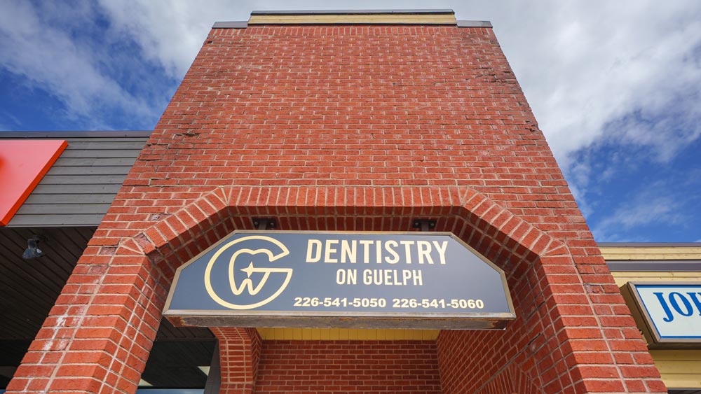 Dentistry on Guelph sign on a red brick building under a blue sky.