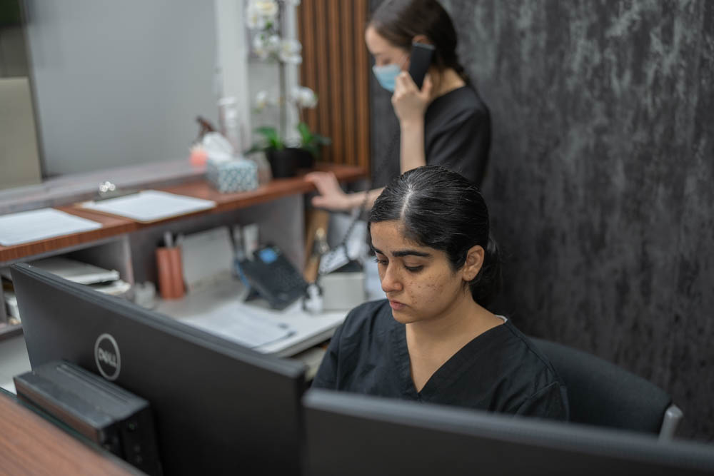 Two women in scrubs working at a reception desk with computers.