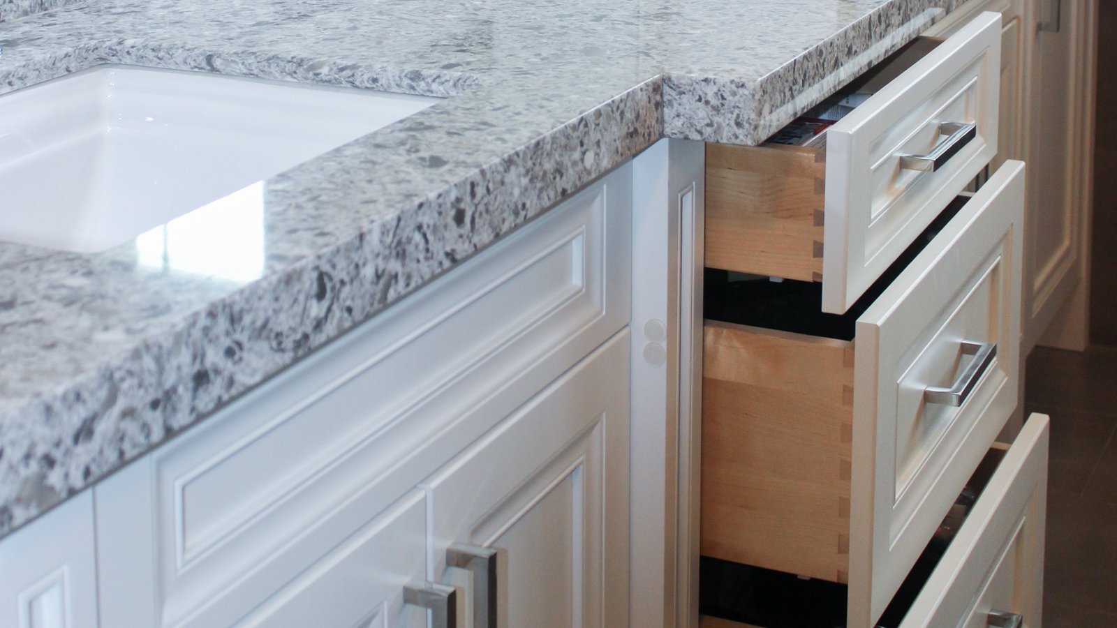 Close-up of white kitchen cabinets with granite countertop and open drawers.