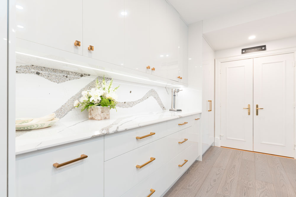 Modern white kitchen with quartz countertops and brass hardware.