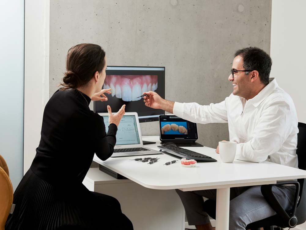 Dentist and patient review digital dental scans on computer screens.