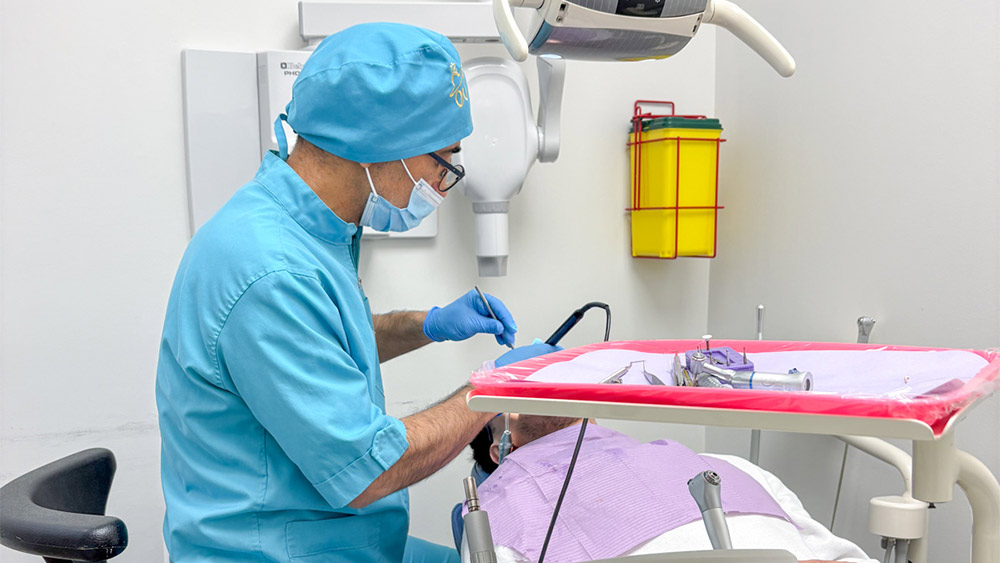 Dr. Reza Shahhaidari, DDS in blue scrubs and mask working on a patient's teeth.