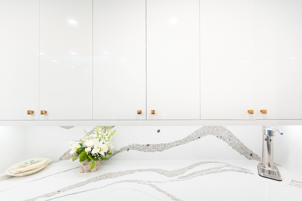 Modern white kitchen cabinets with wood handles and a quartz countertop.