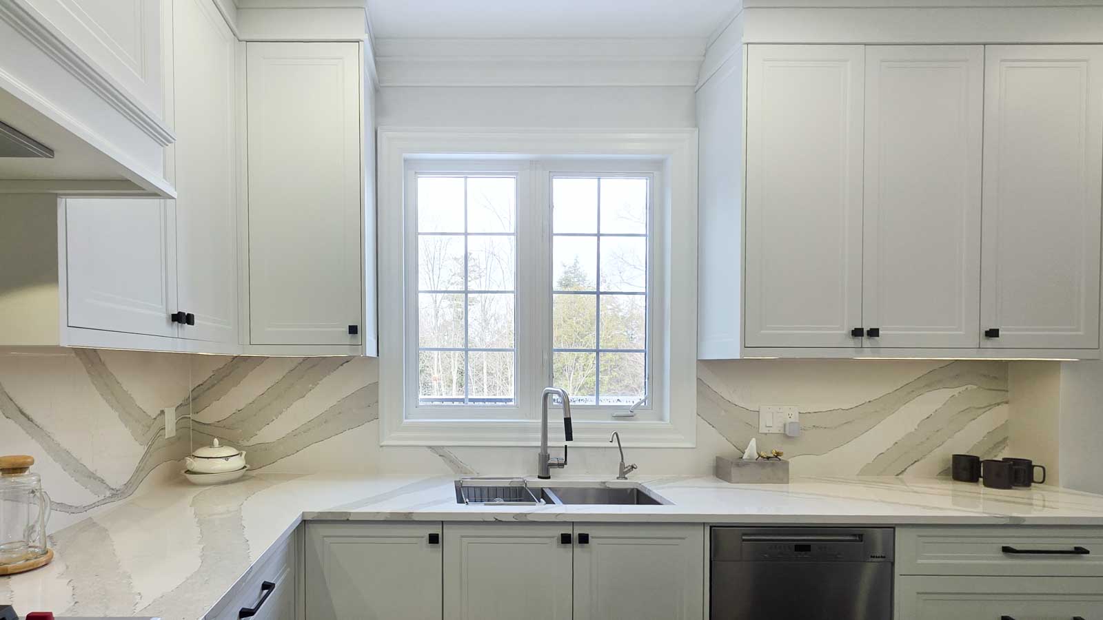 Modern white kitchen with marble backsplash and double window above sink.