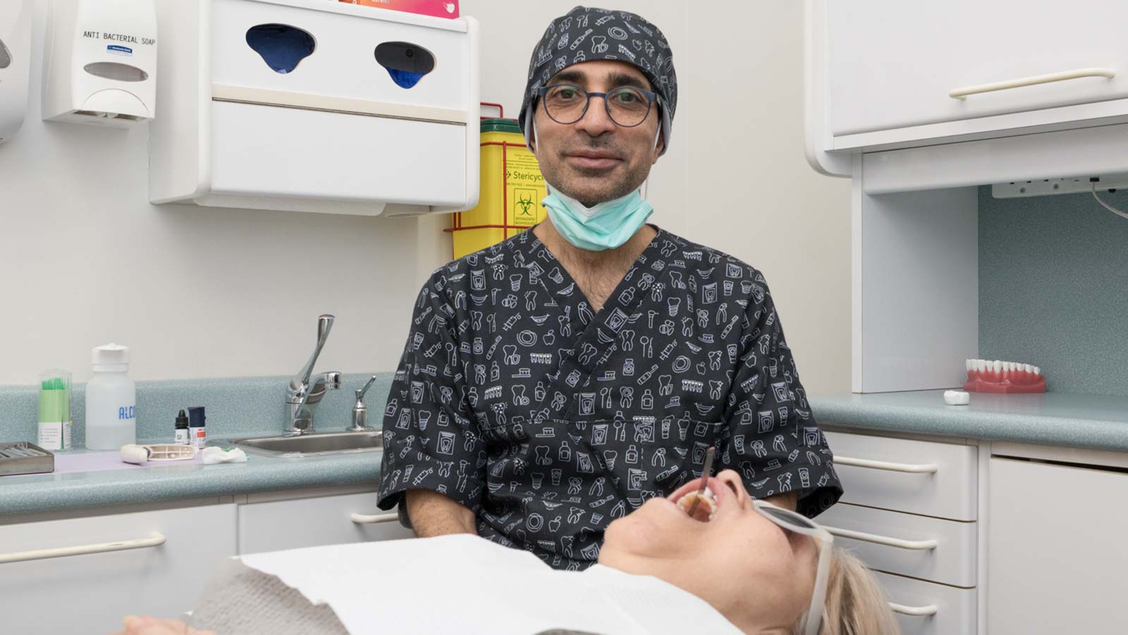 Dr. Reza Shahhaidari in scrubs and cap looks at patient in dental chair.