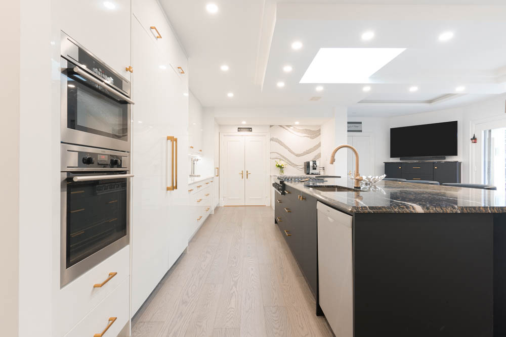Modern white kitchen with a dark island, marble countertop, and gold accents.