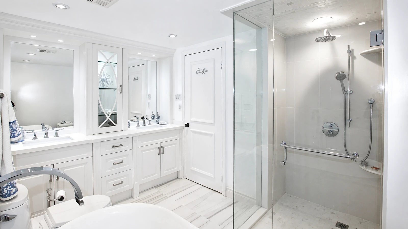 A bright white bathroom with a double vanity and a glass-enclosed shower.