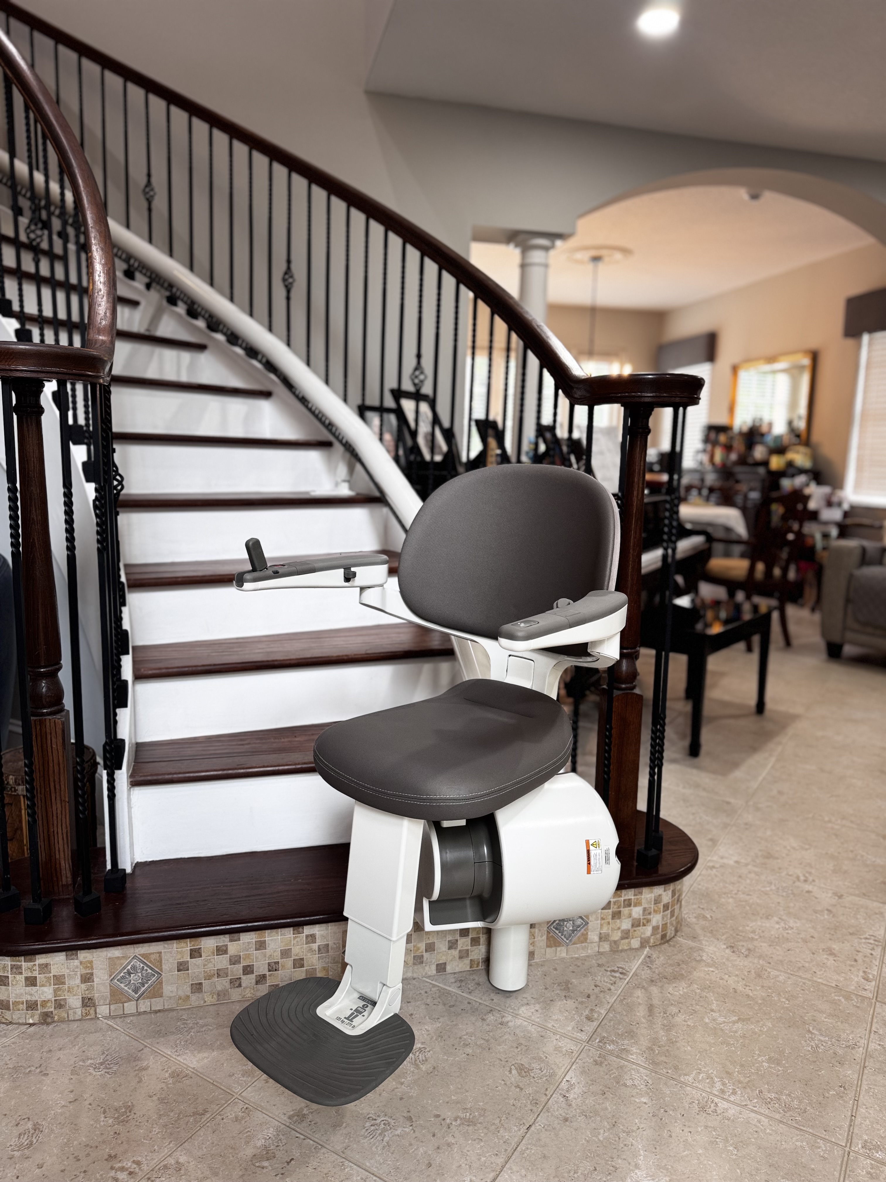 A stair lift chair is installed on a curved staircase in a home.