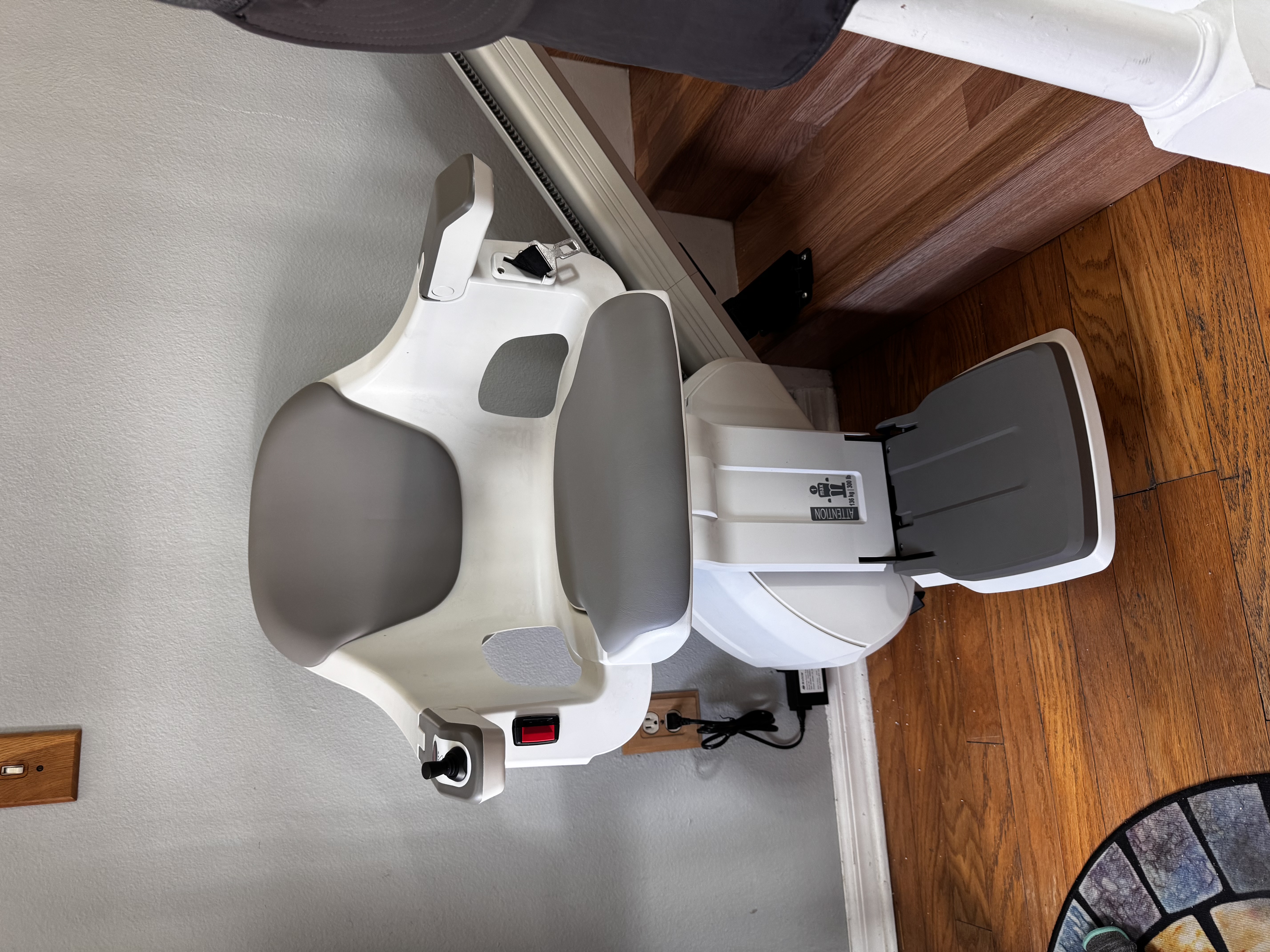 A white and gray stair lift chair is installed on a wooden staircase.