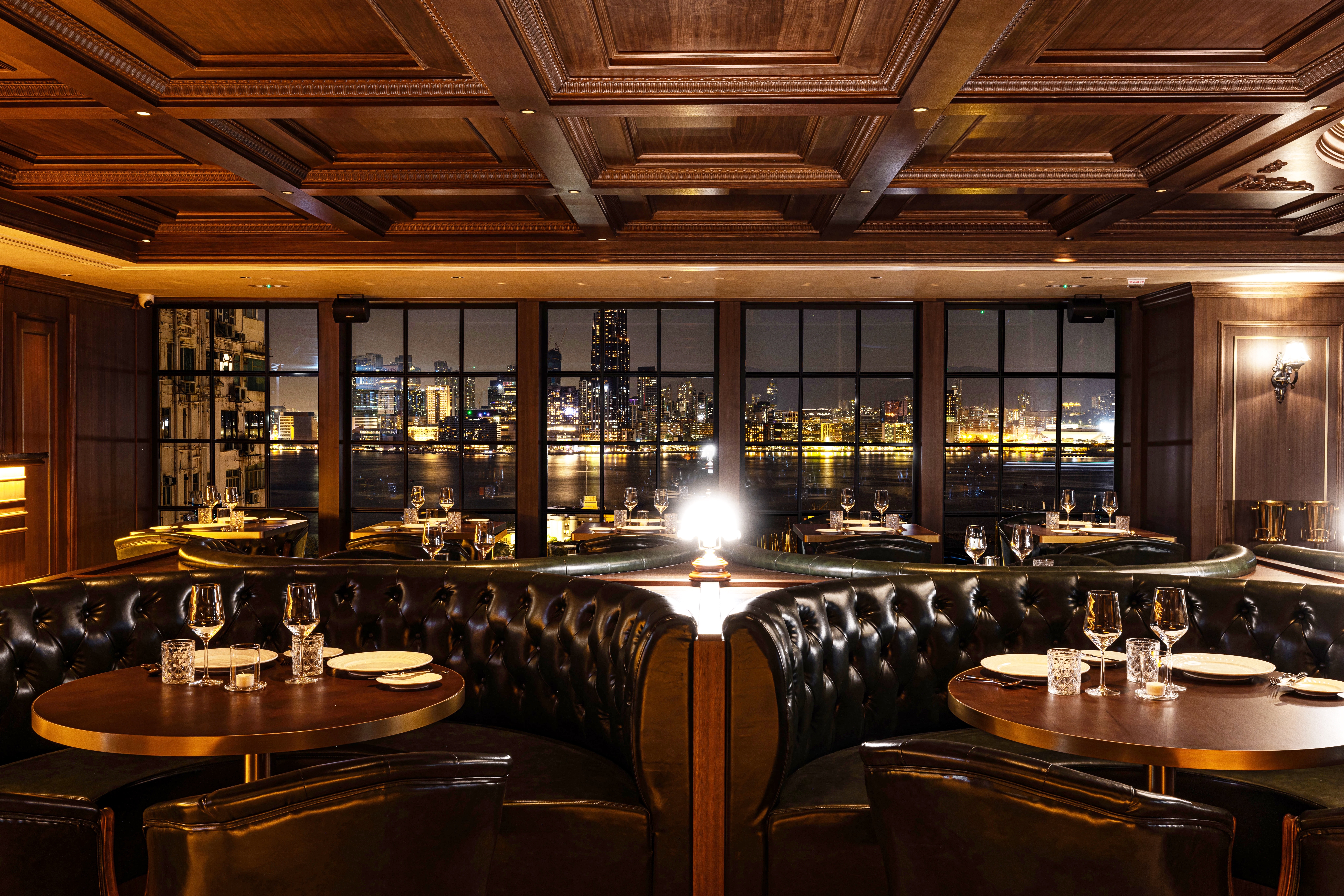 A refined, warm restaurant interior with walnut wood tones and a panoramic view of the harbour, perfect for a special celebration.