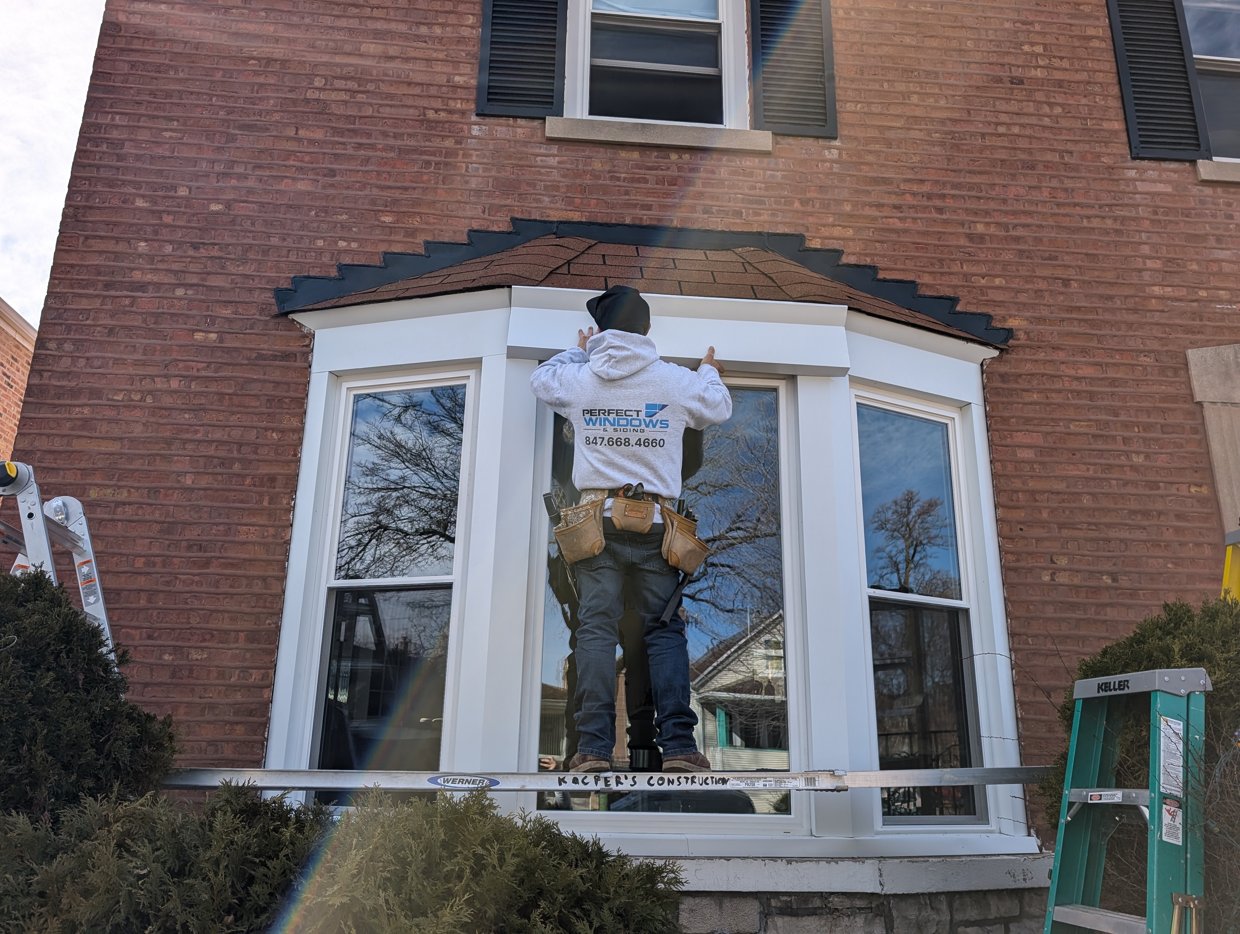 Worker installing new bay window trim on a brick house
