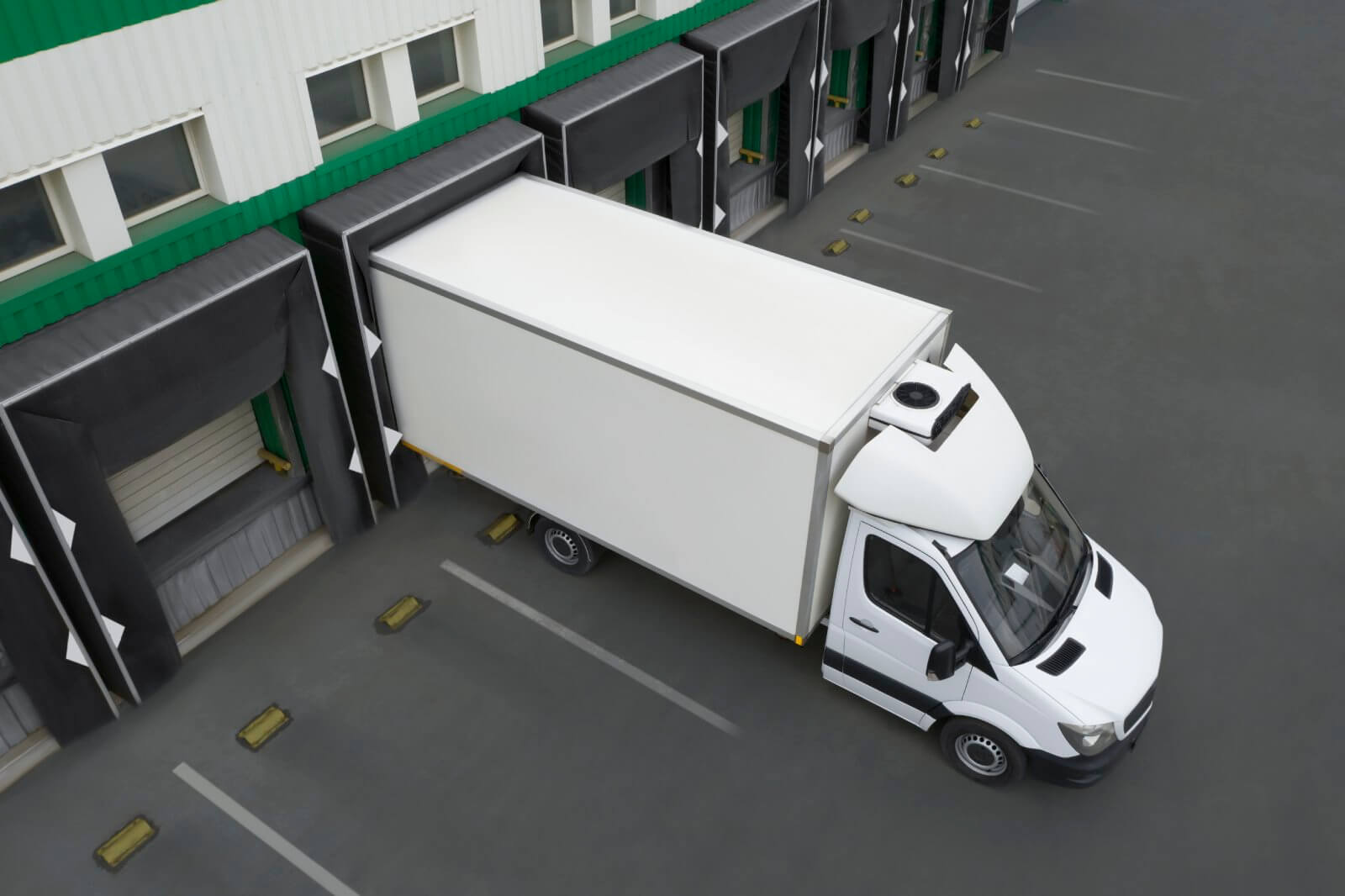 A white truck is parked at a loading dock of a warehouse