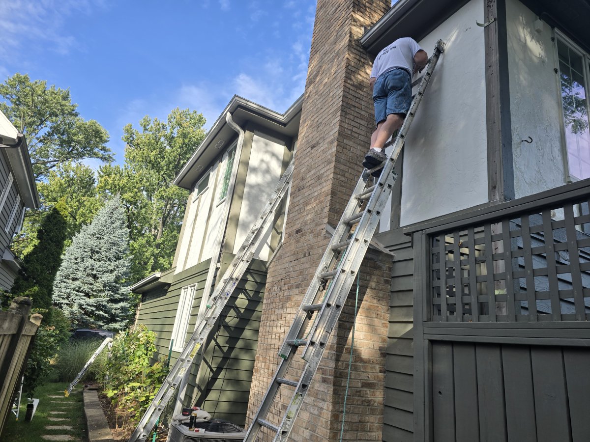 Person on a ladder painting a house exterior
