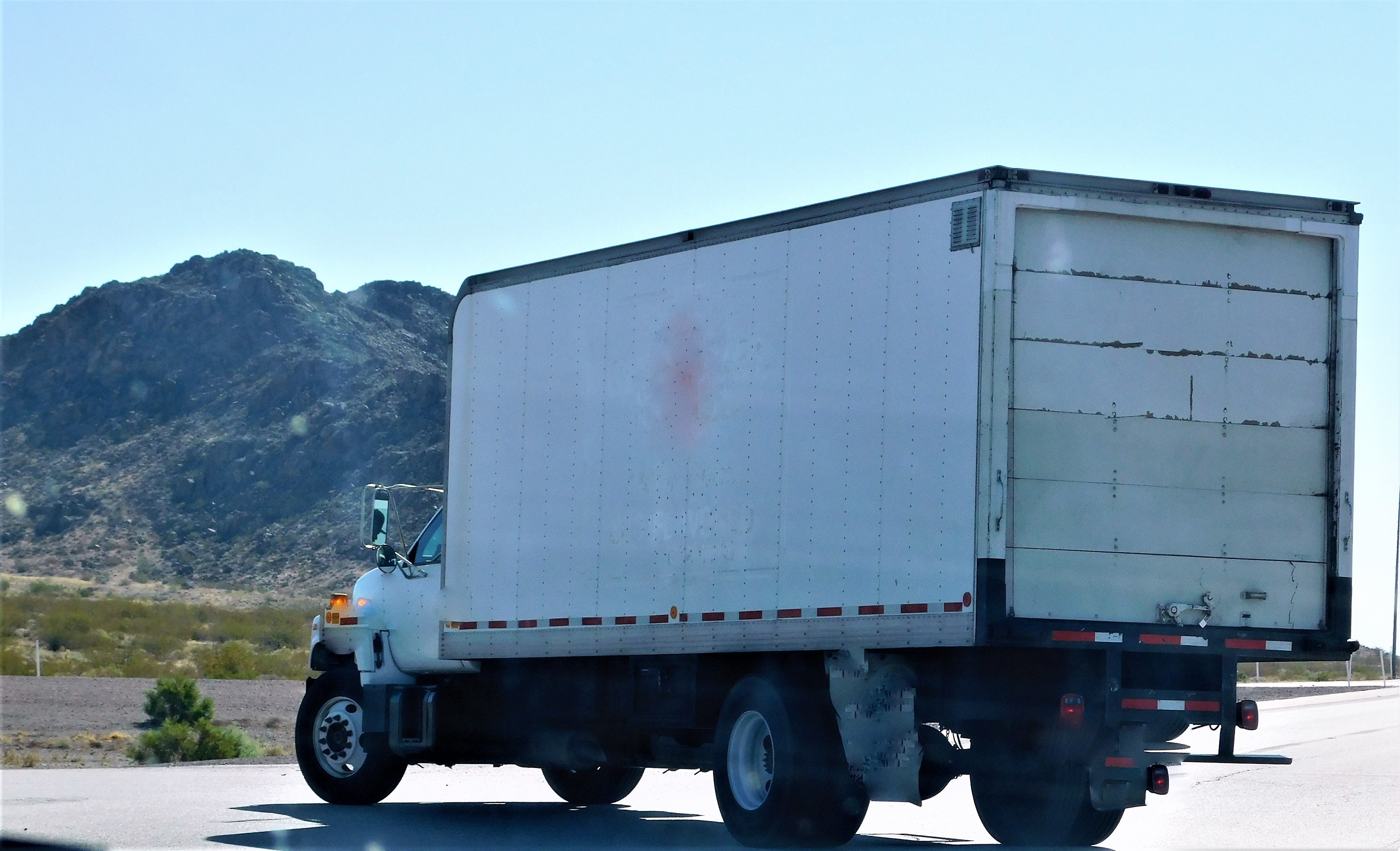 A white box truck drives down a highway with mountains in the background