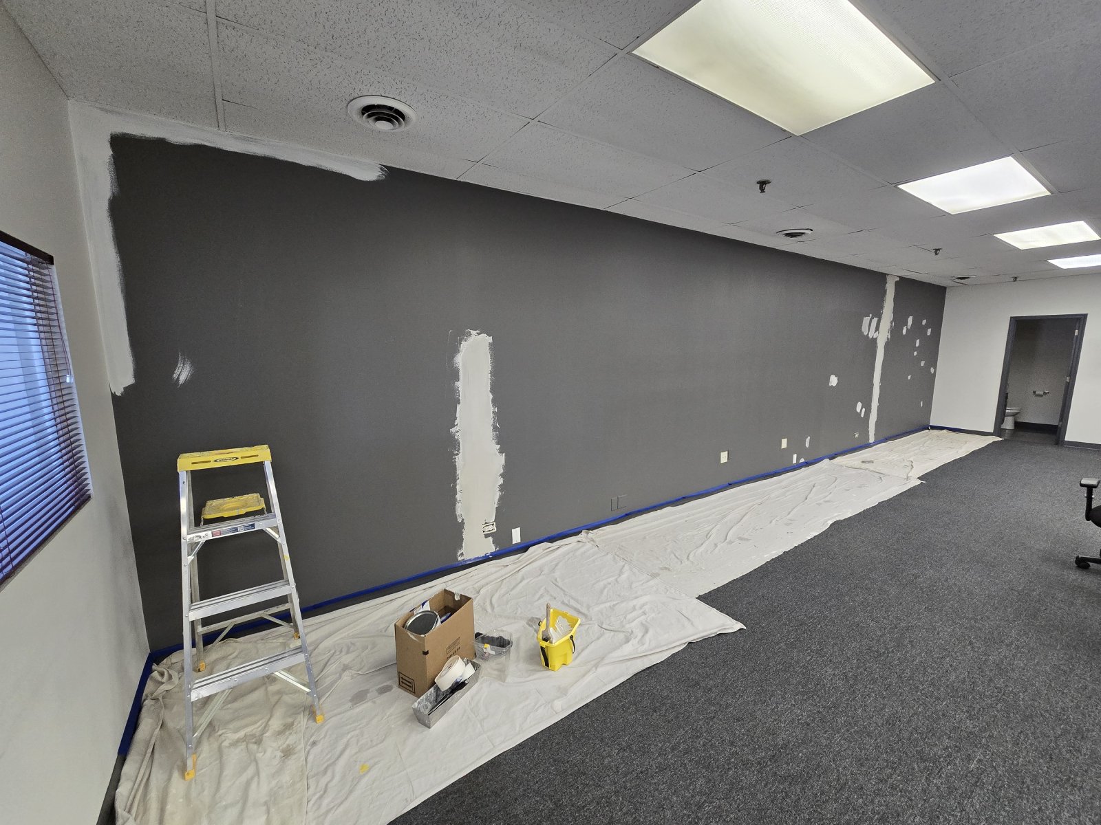 A room is being painted, with a ladder and painting supplies on drop cloths.