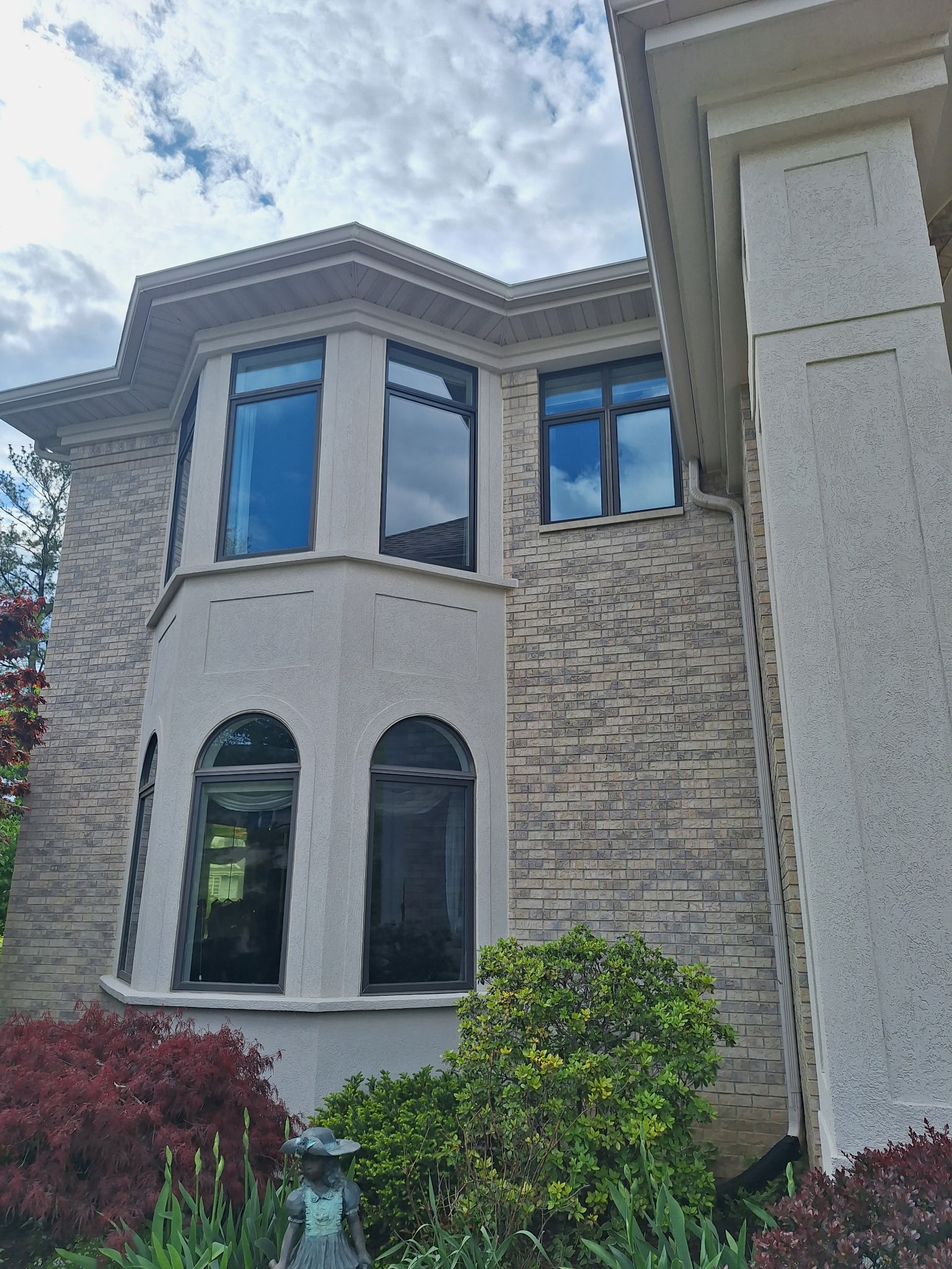 A large house with brick and stucco exterior, bay windows, and landscaping