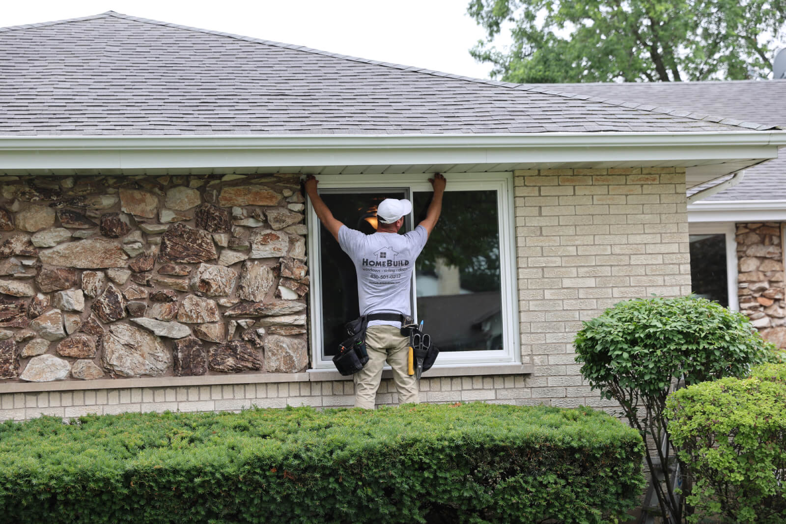 A person installing a window on a house with stone and brick exterior