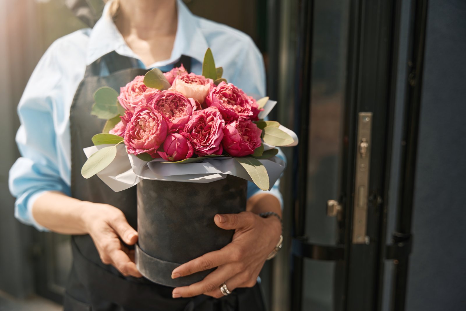 A person holds a round box filled with pink roses and greenery.