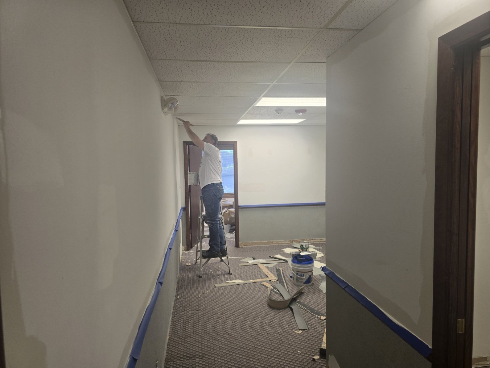 A person is painting a wall in a hallway with blue tape on the walls