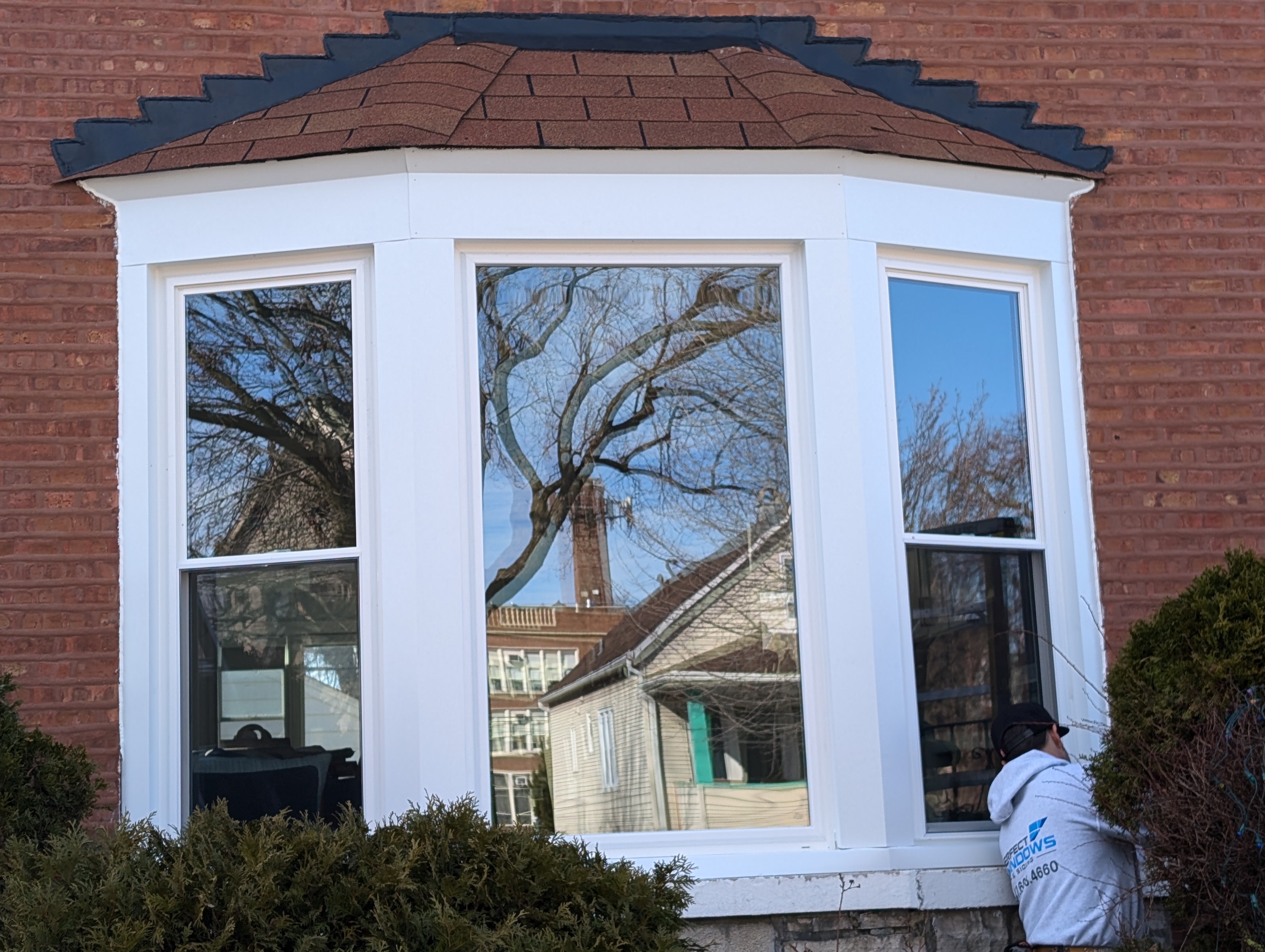 A person works on a bay window on a brick house