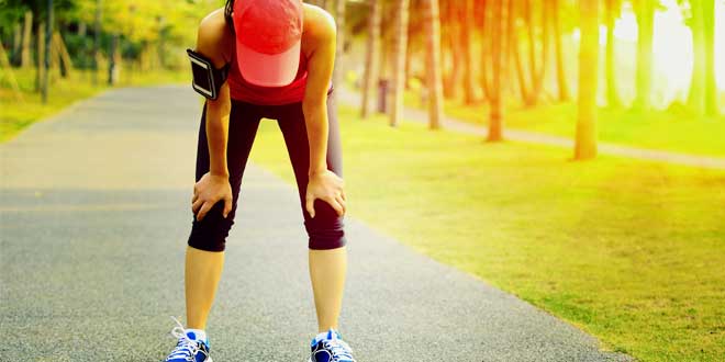 Runner bent over with hands on knees, catching breath on a path.