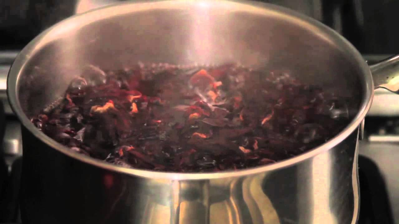 Dark red hibiscus flowers boiling in a silver pot on a stovetop.