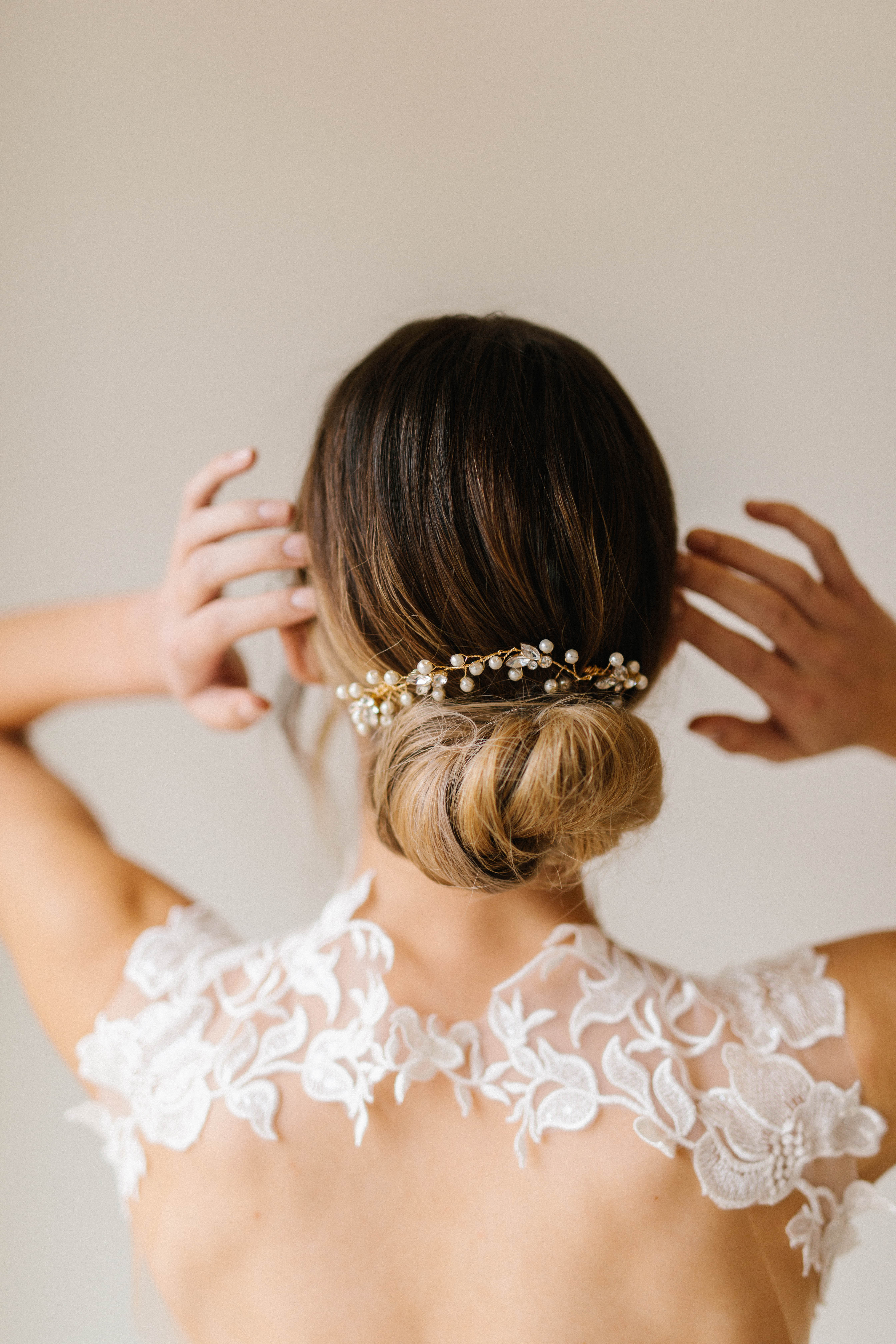 A person with an elegant updo adorned with a pearl and crystal hairpiece.