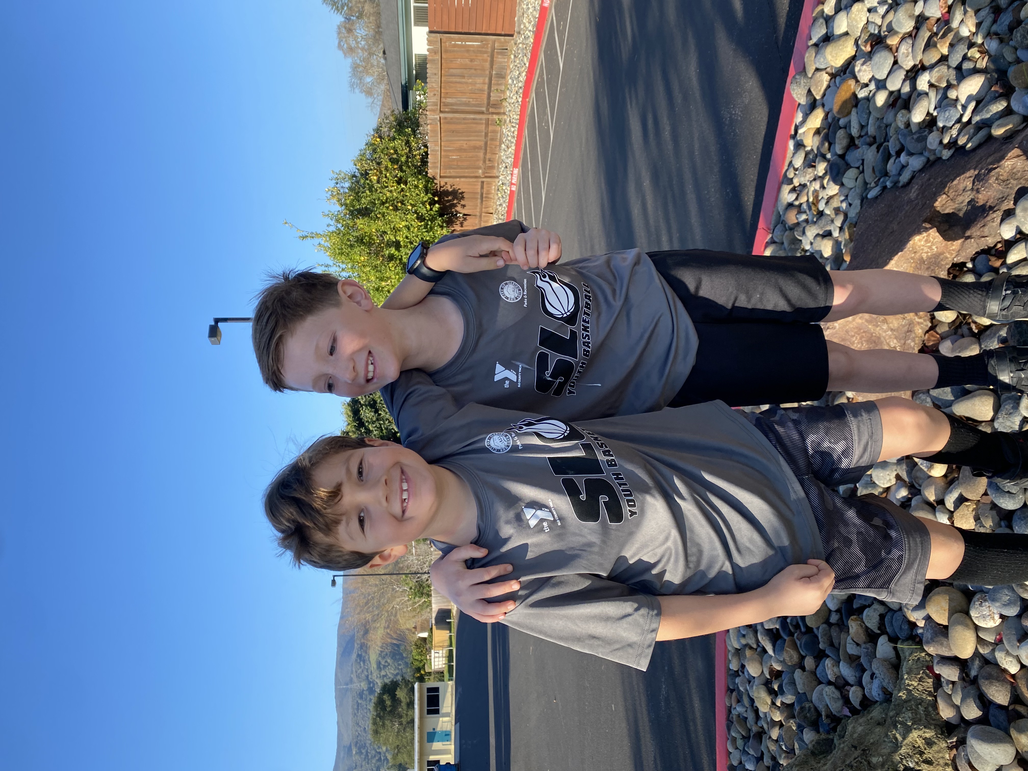 Two smiling children in matching basketball shirts outdoors