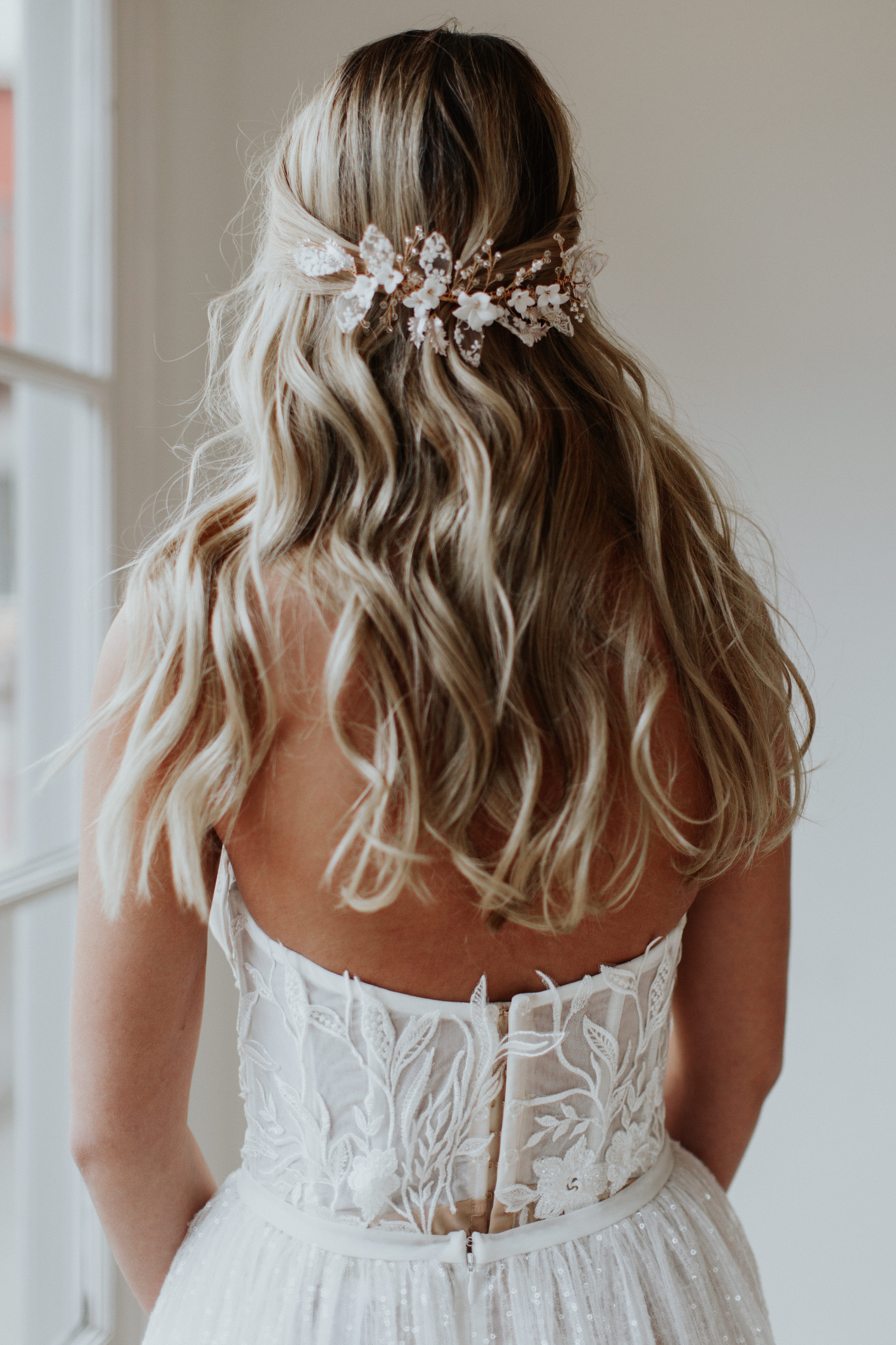A person with blonde hair wearing a white dress and a floral hair accessory.