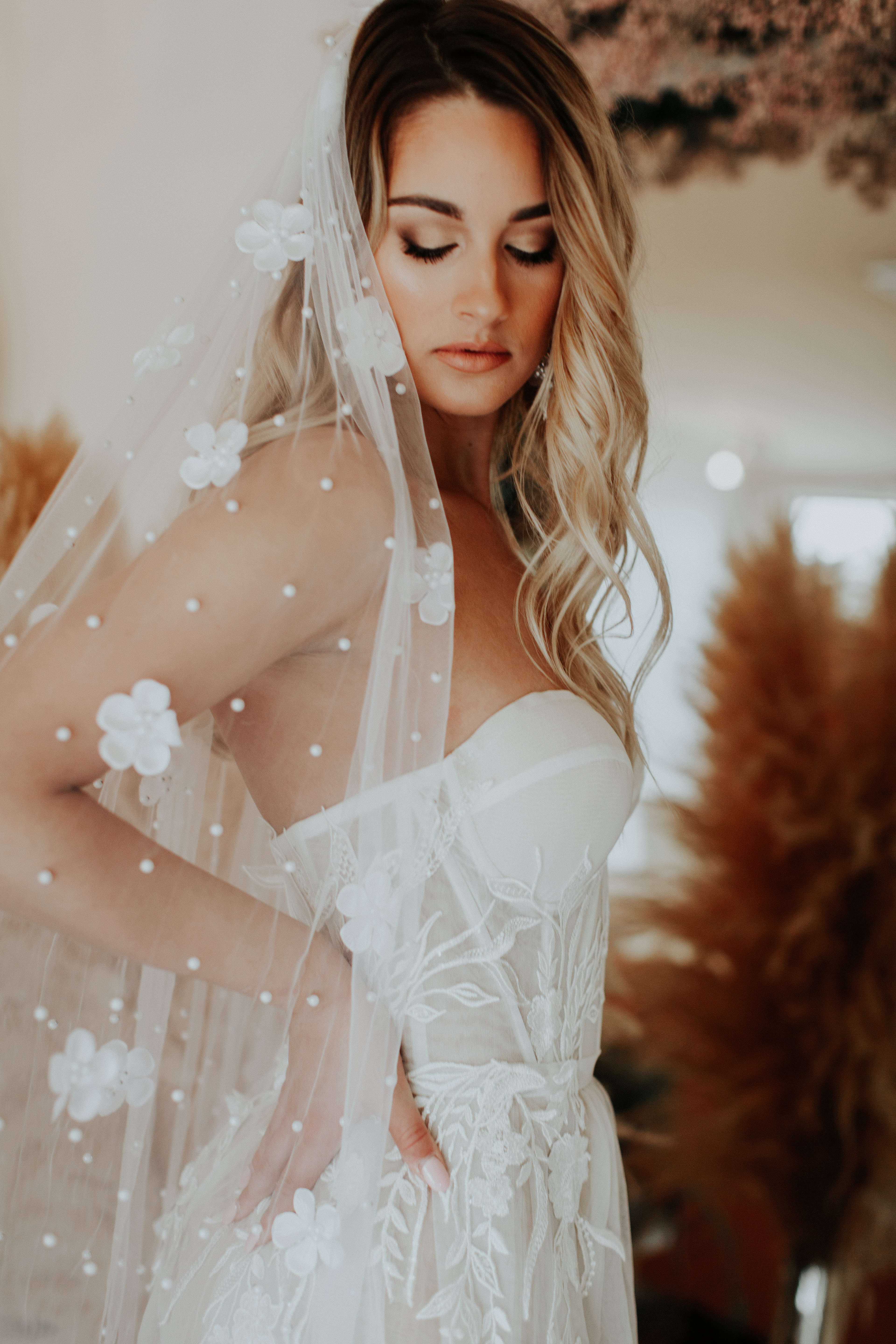 A bride in a white dress and veil with floral embellishments.
