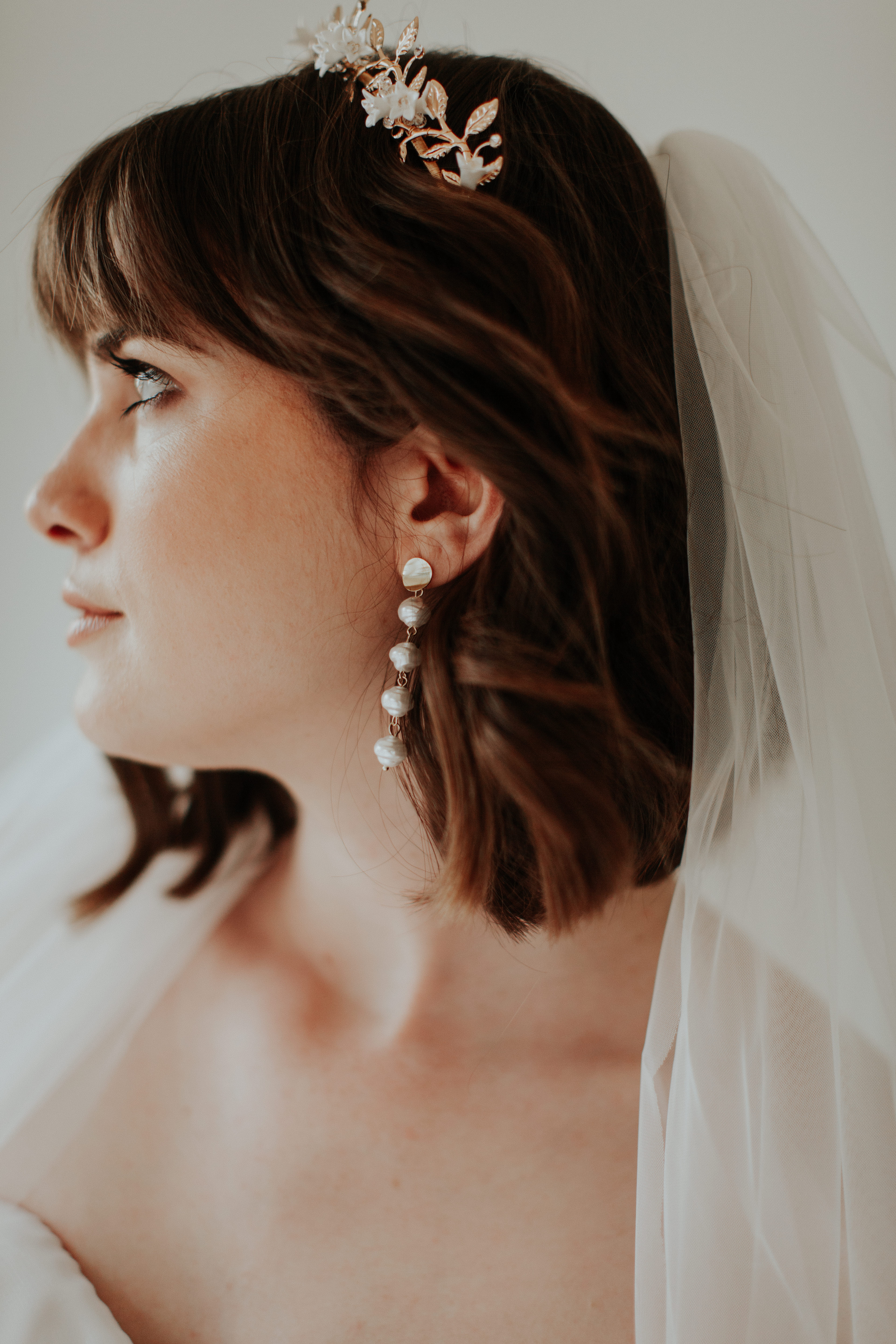 A bride wears a tiara and pearl earrings with a veil.