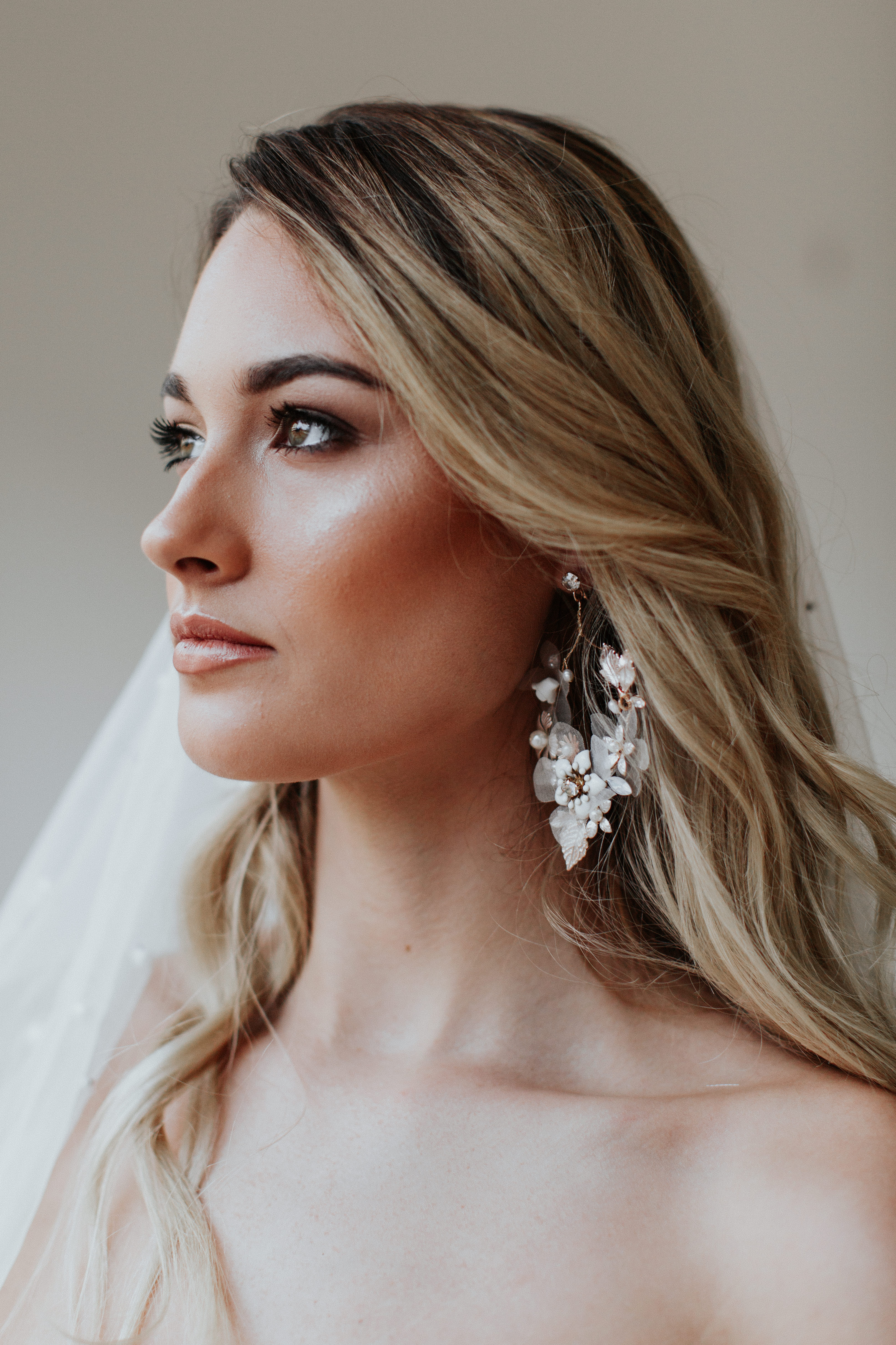 A woman with blonde hair and large floral earrings, wearing a veil.