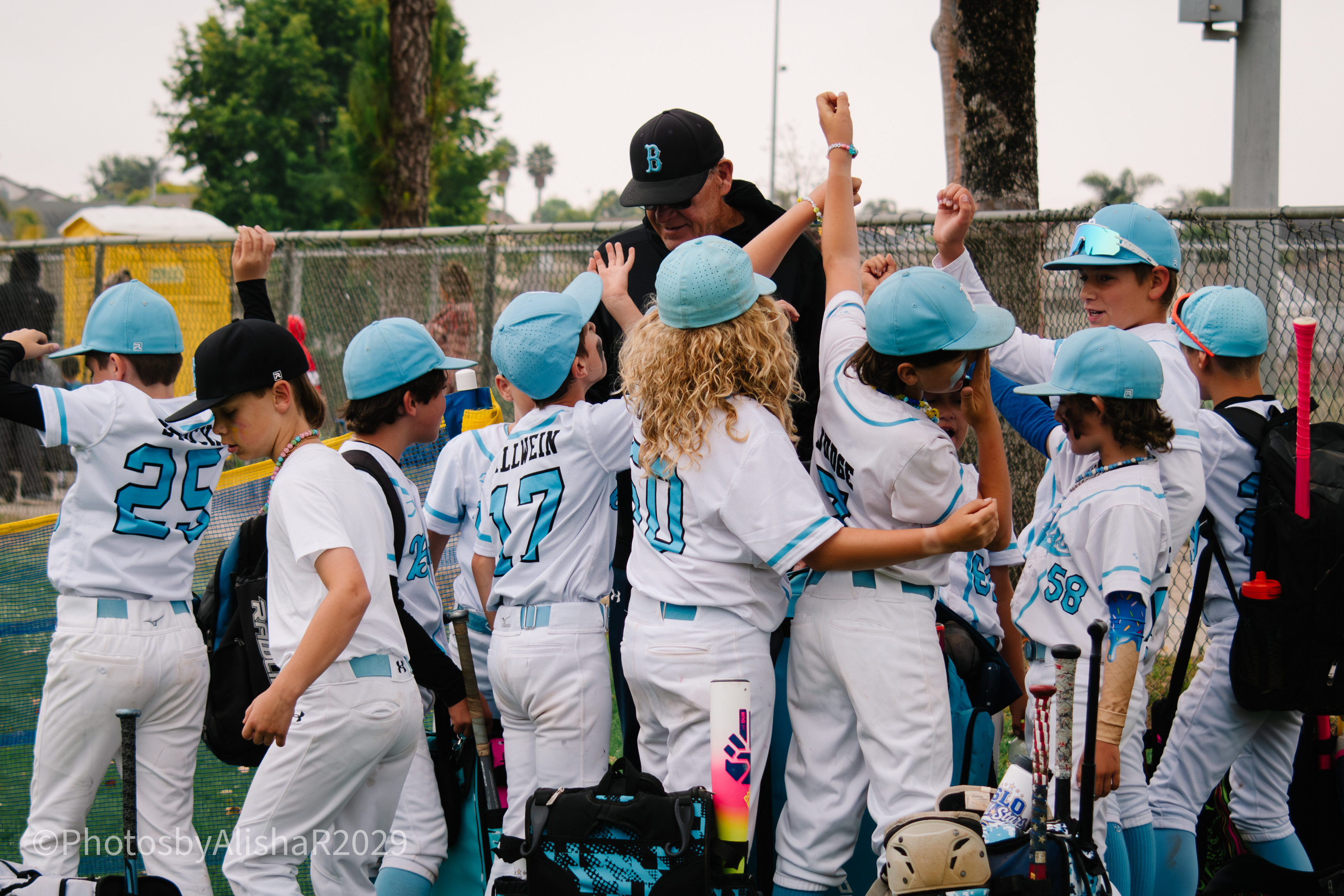 A group of young baseball players in uniform celebrating with a coach.