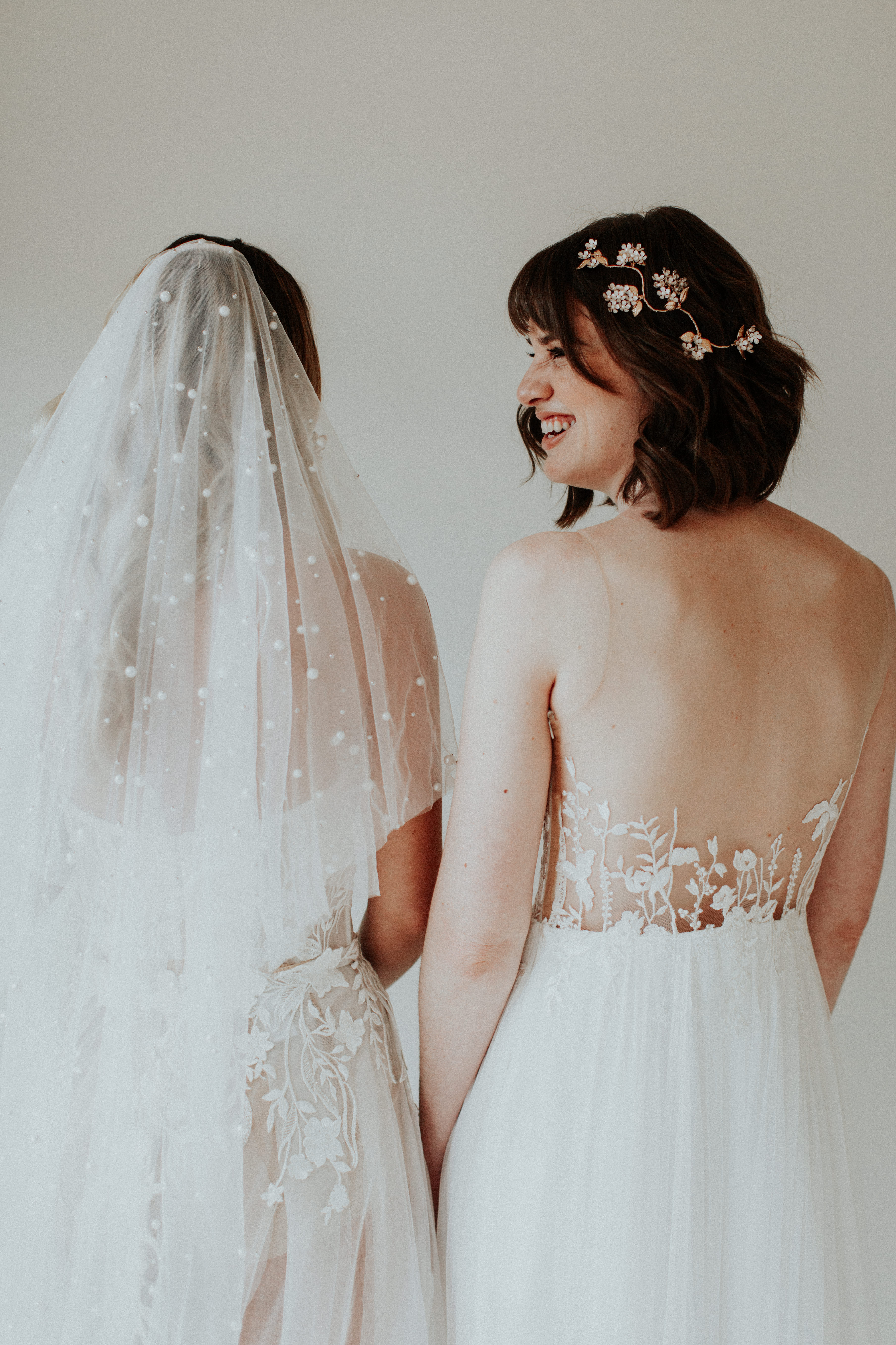 Two people in wedding dresses, one with a pearl veil.