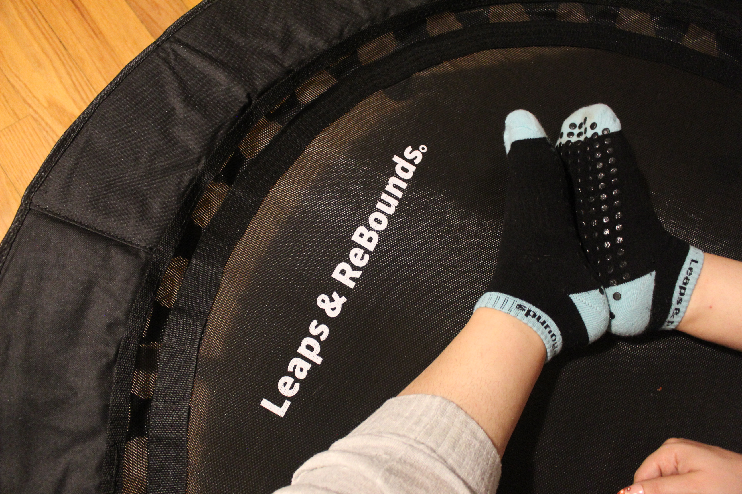 Person wearing grip socks sitting on a mini trampoline, indoors