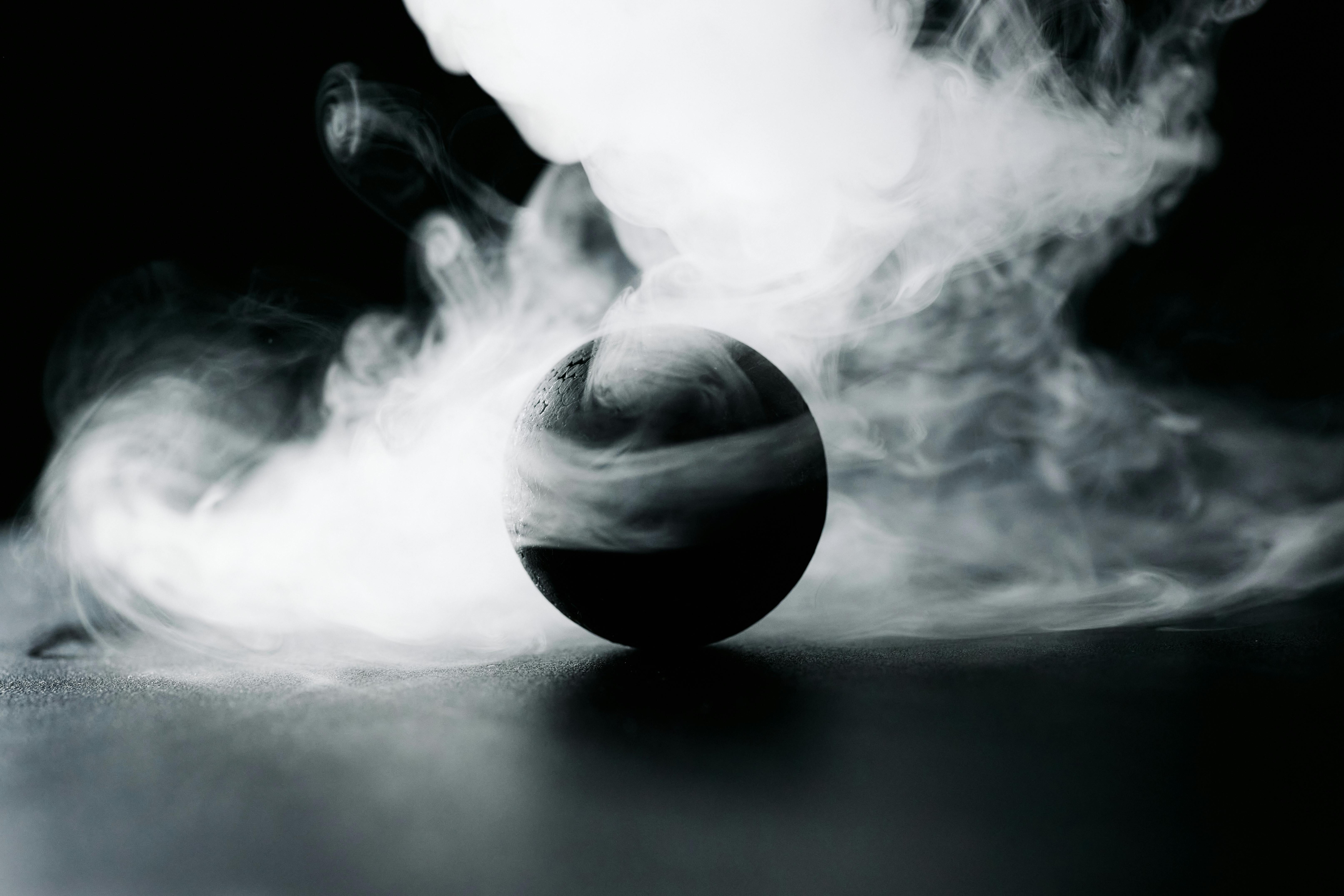 A dark sphere surrounded by swirling white smoke on black background.